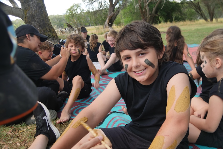 A boy painted in ochre smiles at the camera