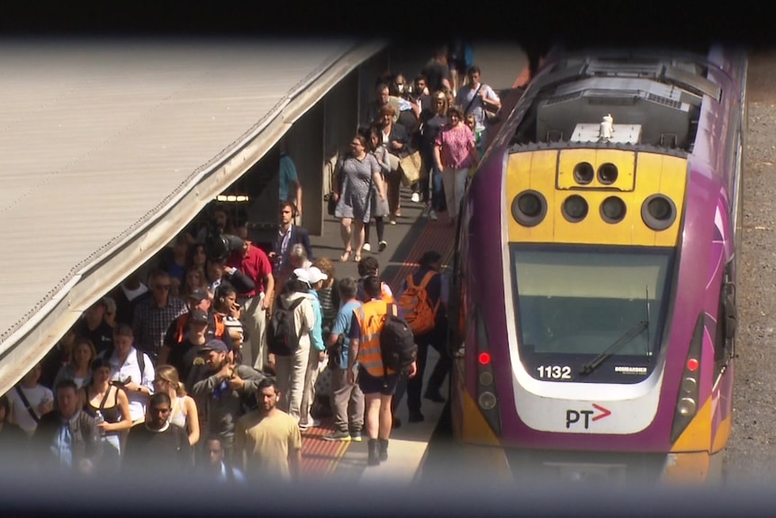 Dozens of commuters getting on and off a V/Line train at a Melbourne platform.
