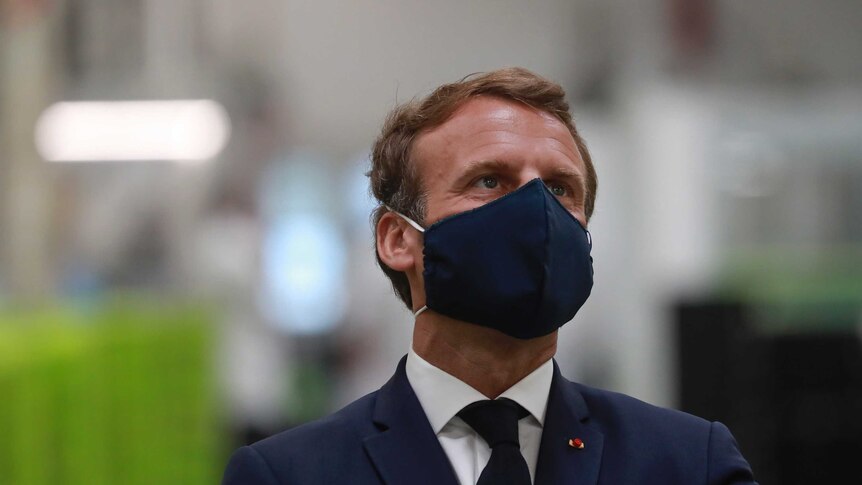 French President Emmanuel Macron wears a face mask as he visits a factory.