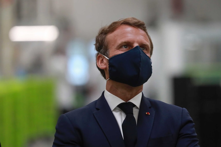 French President Emmanuel Macron wears a face mask as he visits a factory.