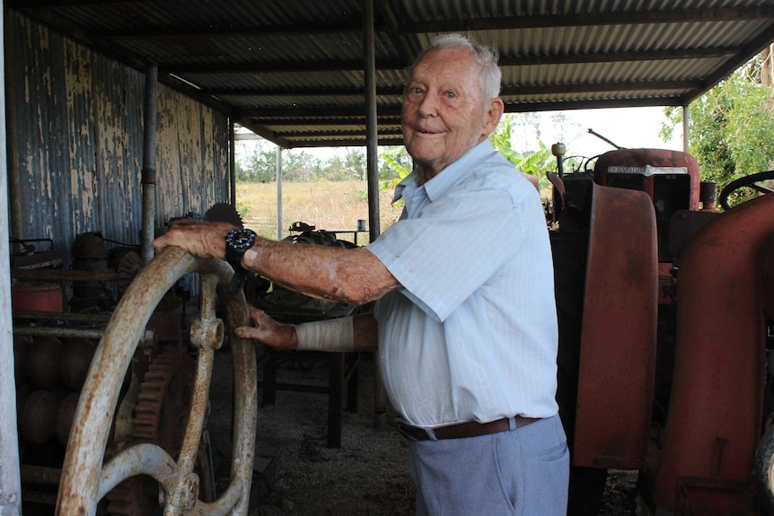 A man with his hands on an old rusty steering wheel smiling in front of old farming equipment