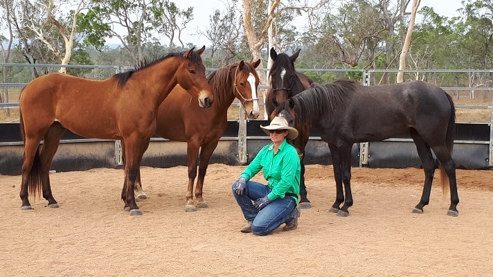 Rebecca kneels in a green shirt in front of four horses.