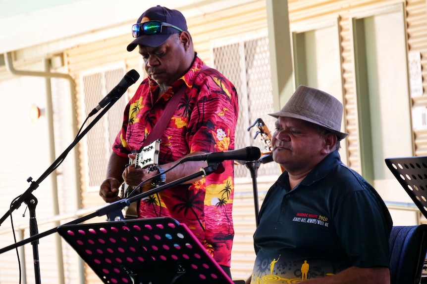 Two men stand on a stage playing music.