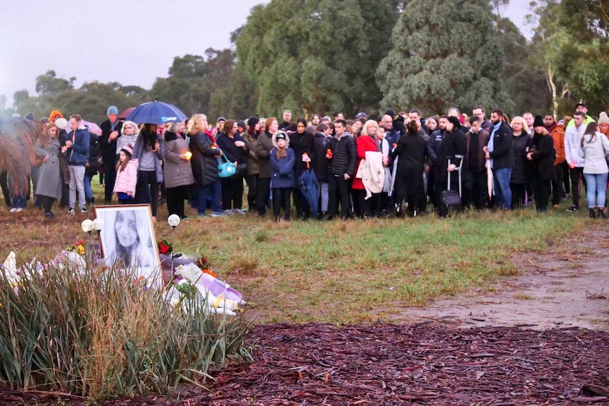 A group of people standing behind a photo of Courtney Herron and bunches of flowers.