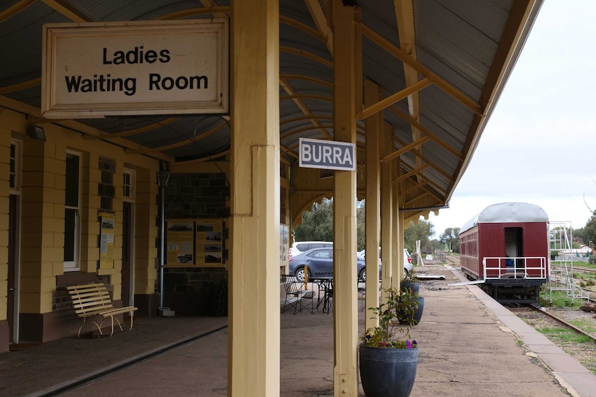 The maroon painted dining carriage sits next to the waiting area that has signage for tourists explaining the history.