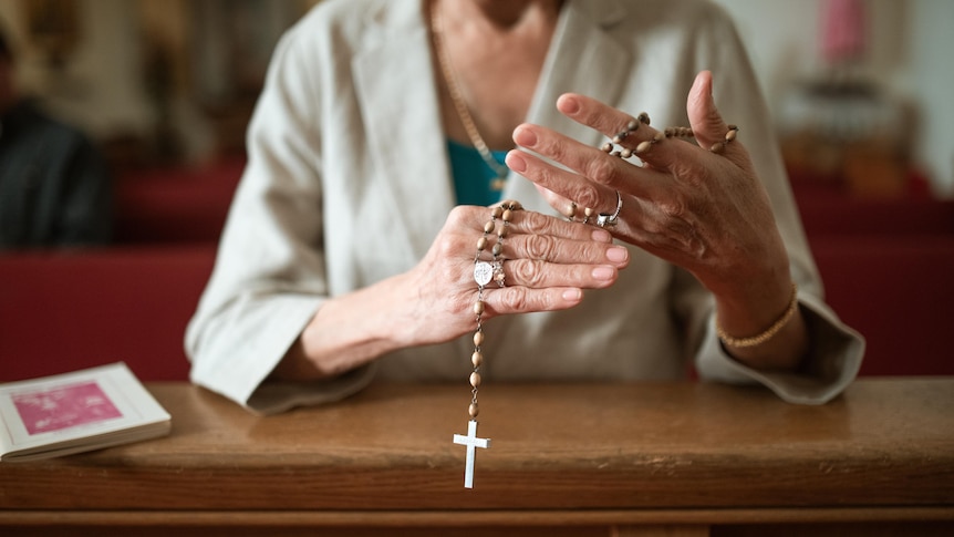 A woman in a white jacket with beads over her hands and a cross at the end