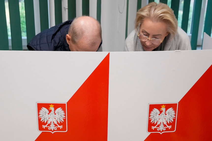 Two people behind a voting box with the Polish emblem on it. 