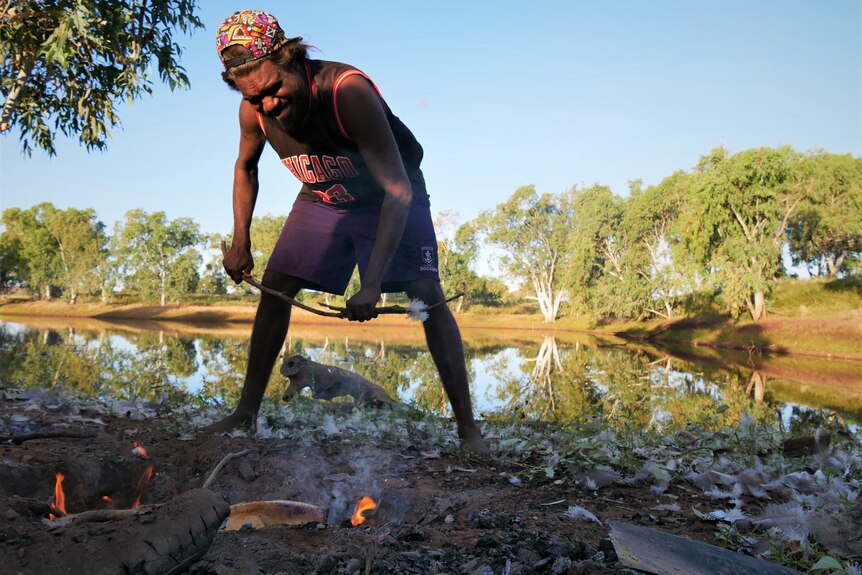 Aboriginal man Felix Williams tends to a fire cooking an Australian bustard 