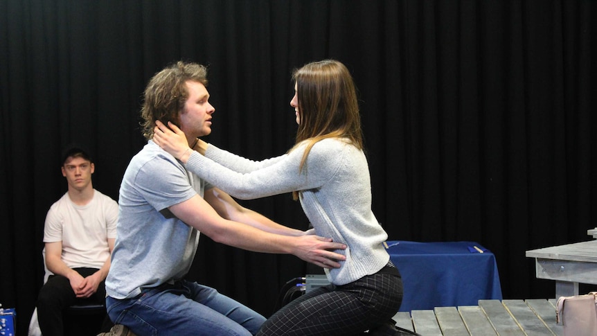 Two actors kneeling on stage with their arms around each other.