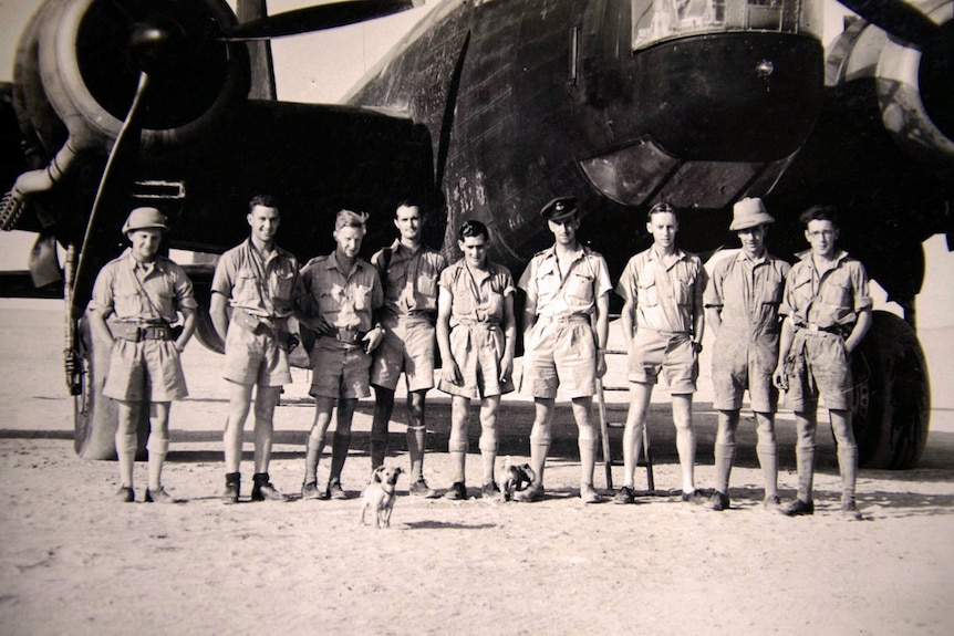 A group of nine men standing in front of a Wellington bomber in the desert.