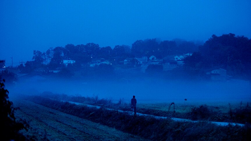 Colour still of Yoo Ah-in jogging in dark blue tinted at night time in rural Paju in 2018 film Burning.