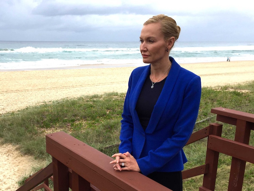A woman in a blue business suit stands near a beach