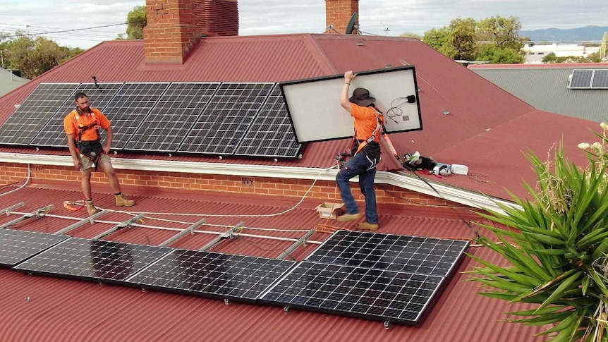 A workman carries a solar panel on a rooftop.