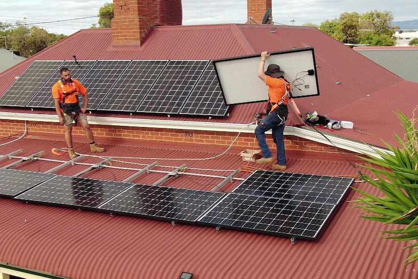 A workman carries a solar panel on a rooftop.