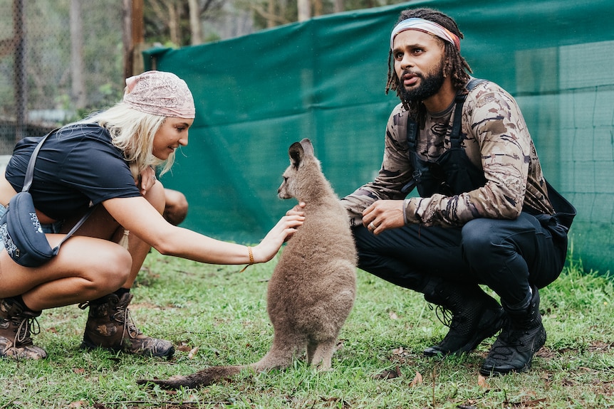 Patty crouches down with a wallaby and another person who's patting the wallaby.