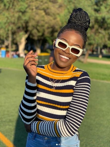 Elsy Wameyo smiling while wearing white sunglasses and a stripy jumper
