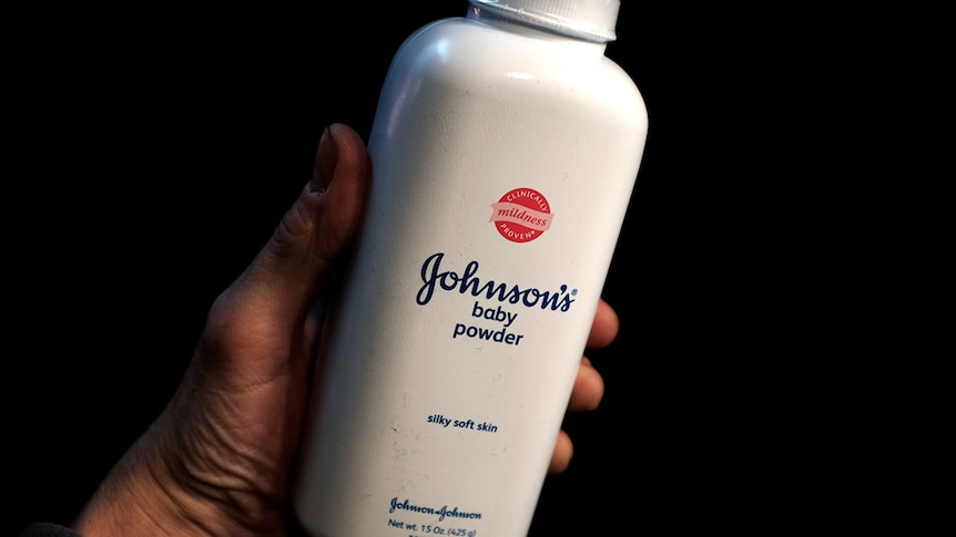 A hand holding a white bottle of johnson and johnson baby powder 