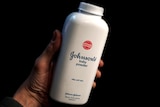 A hand holding a white bottle of johnson and johnson baby powder 