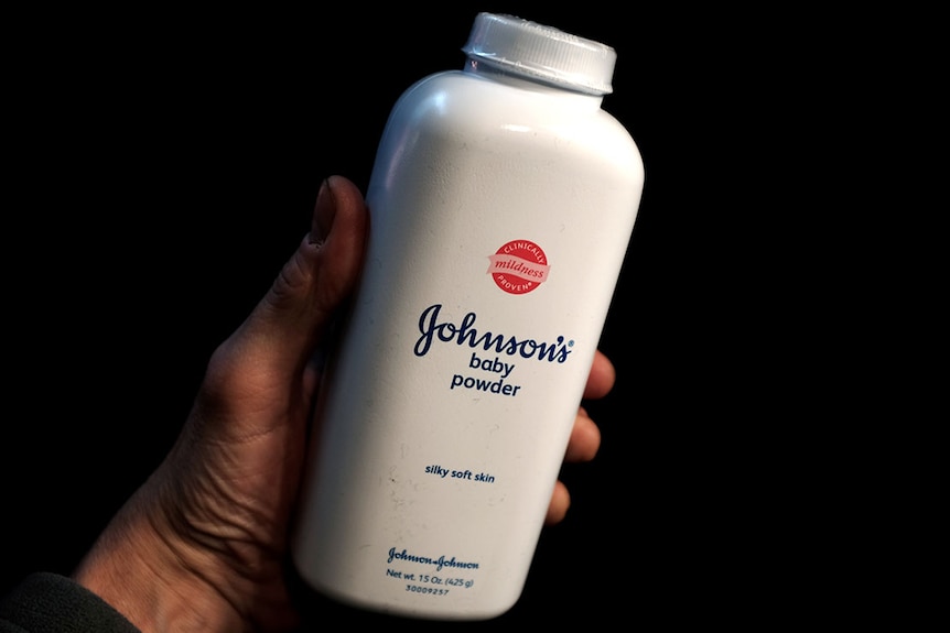 A hand holding a white bottle of johnson and johnson baby powder 