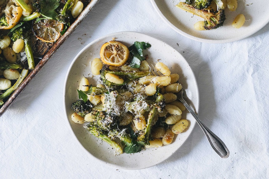 A bowl of baked gnocchi, broccoli and lemon topped with grated pecorino cheese, an easy vegetarian dinner for families.