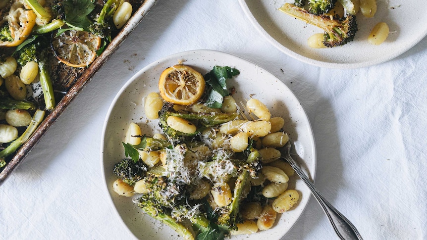 A bowl of baked gnocchi, broccoli and lemon topped with grated pecorino cheese, an easy vegetarian dinner for families.