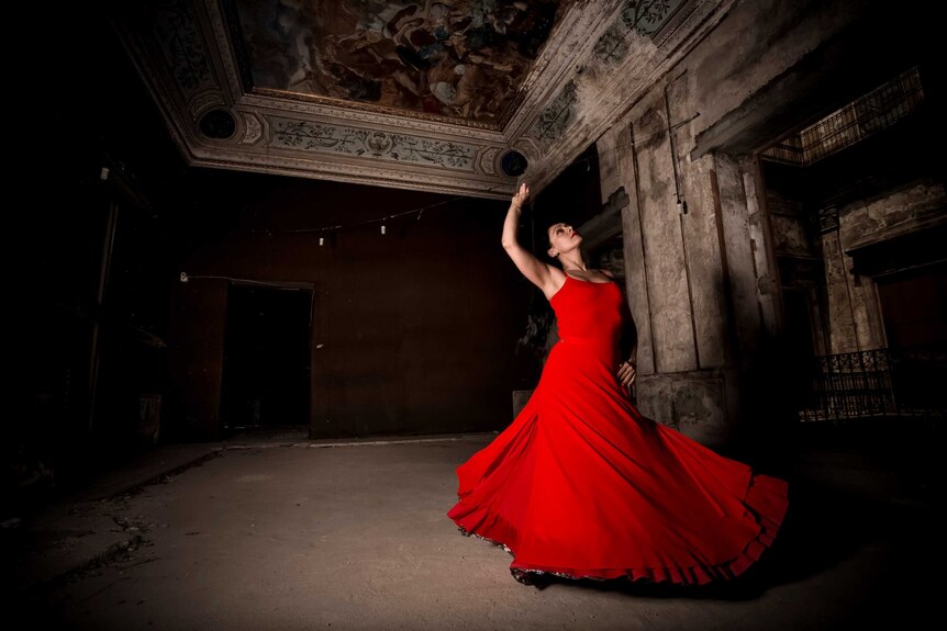 A woman holds up one arm as she spins in a red dress.
