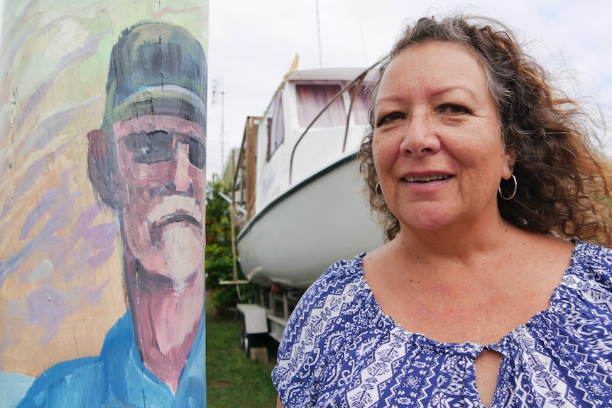 A woman smiles next to a painting of a man on a power pole