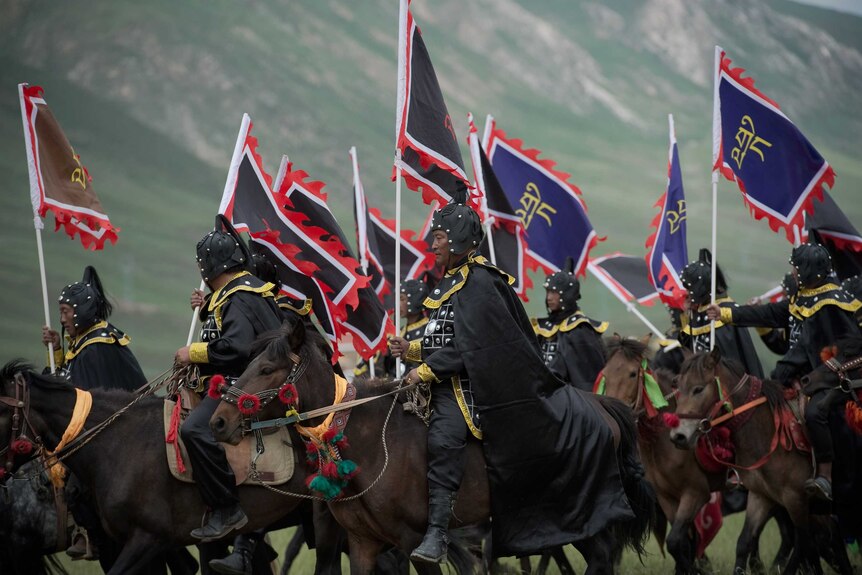 Ethnic Tibetans riding horses in traditional dress with flags