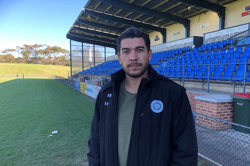 Mark Gerrard stands in front of seats at a football field.