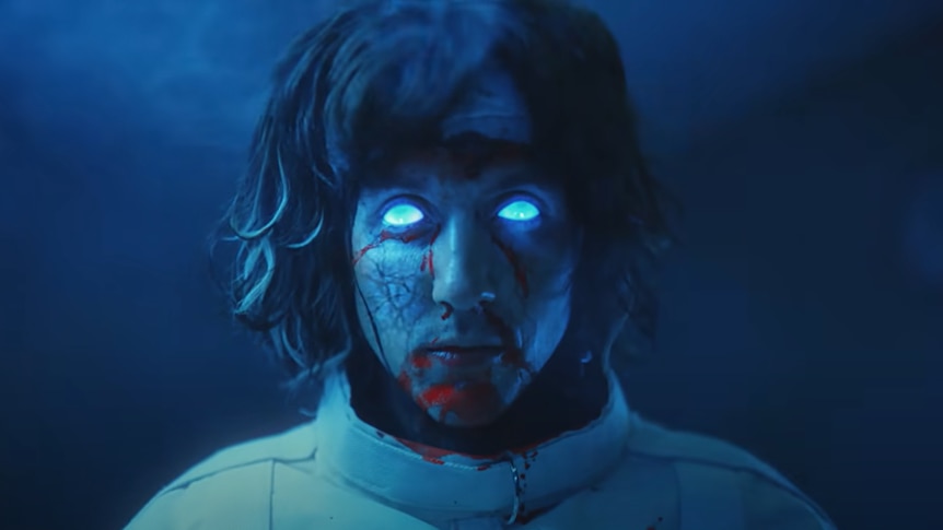 Oliver Sykes from Bring Me The Horizon in the Lost video clip with electric blue eyes and blood splatter on his face.