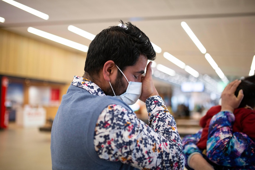 A man in a floral shirt wearing a face mask is visibly moved 