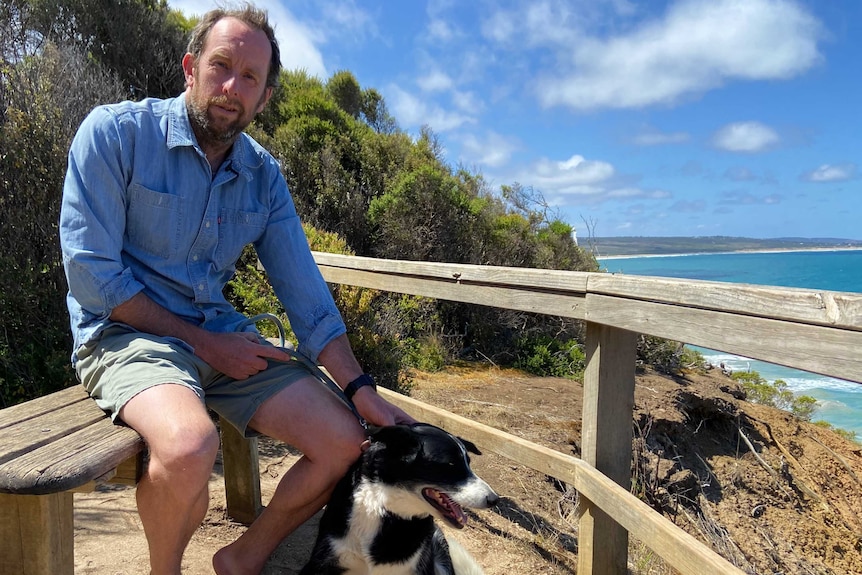 A man patting a dog at a lookout over the ocean.