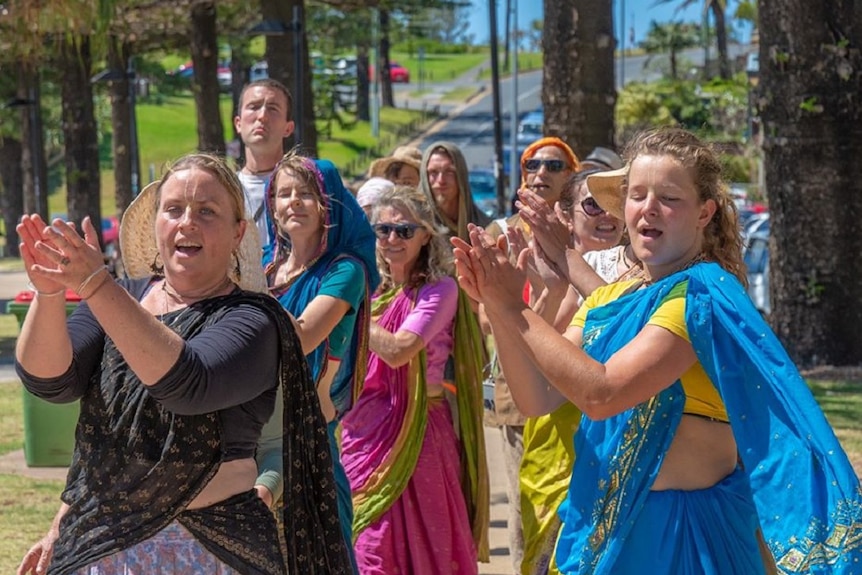 A group of men and women in colourful outfits are dancing and clapping their hands