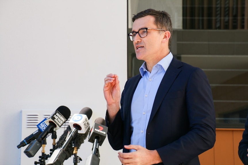 A photo of John Carey standing in front of a bank of microphones.