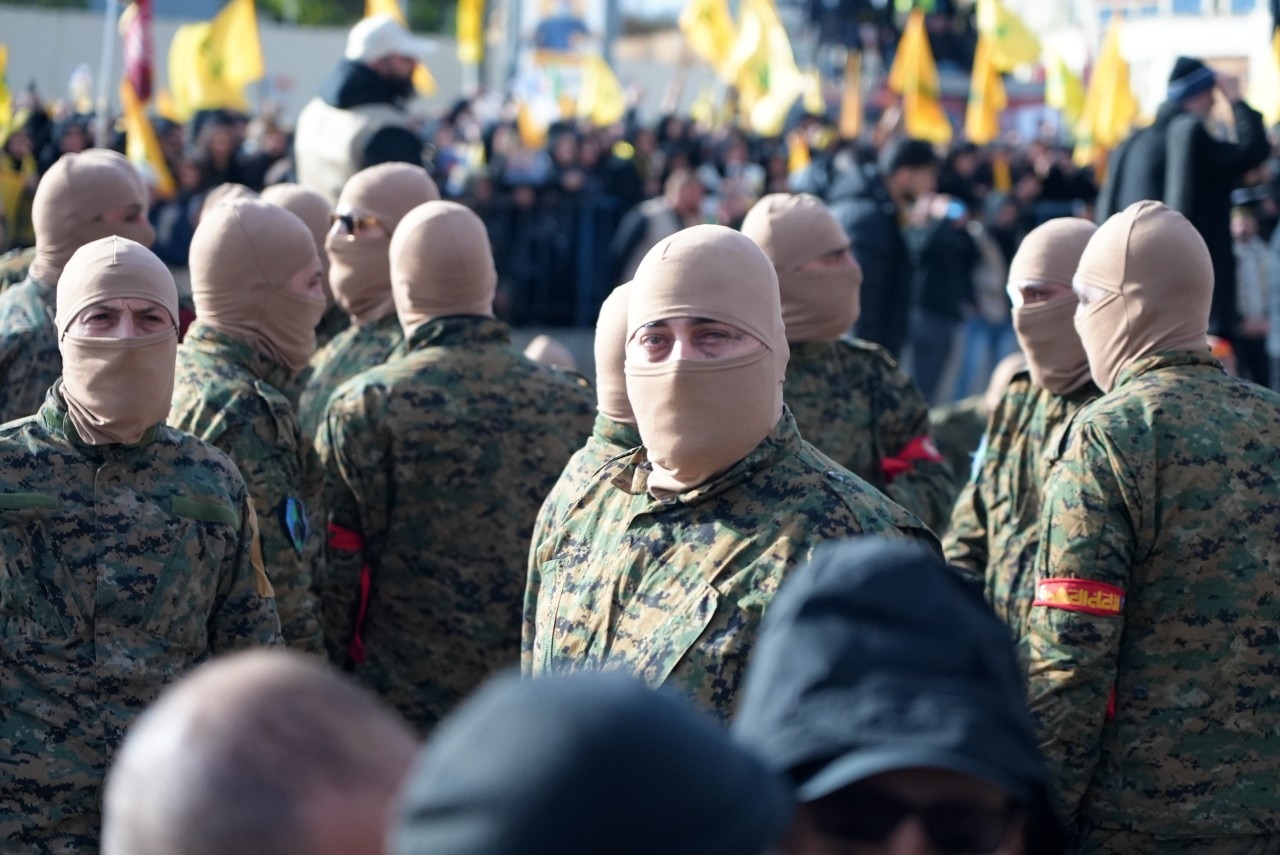 A group of men with their faces covered, looking on.
