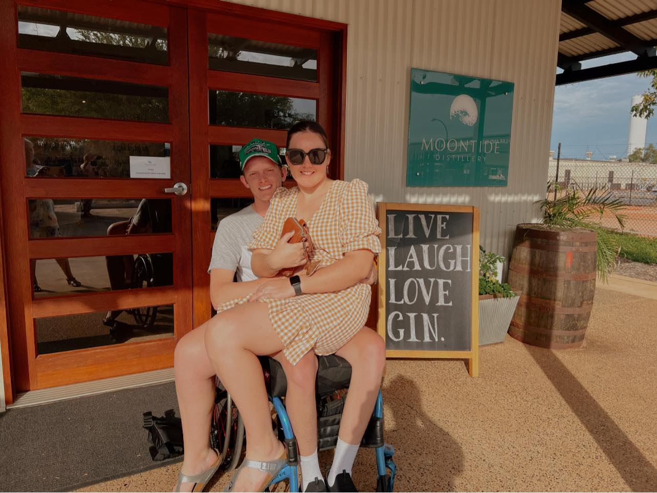 A young woman perches on a man's lap as he sits in a wheelchair.  Both are smiling.