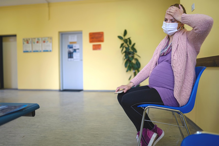 Pregnant woman wearing mask sits in empty waiting room