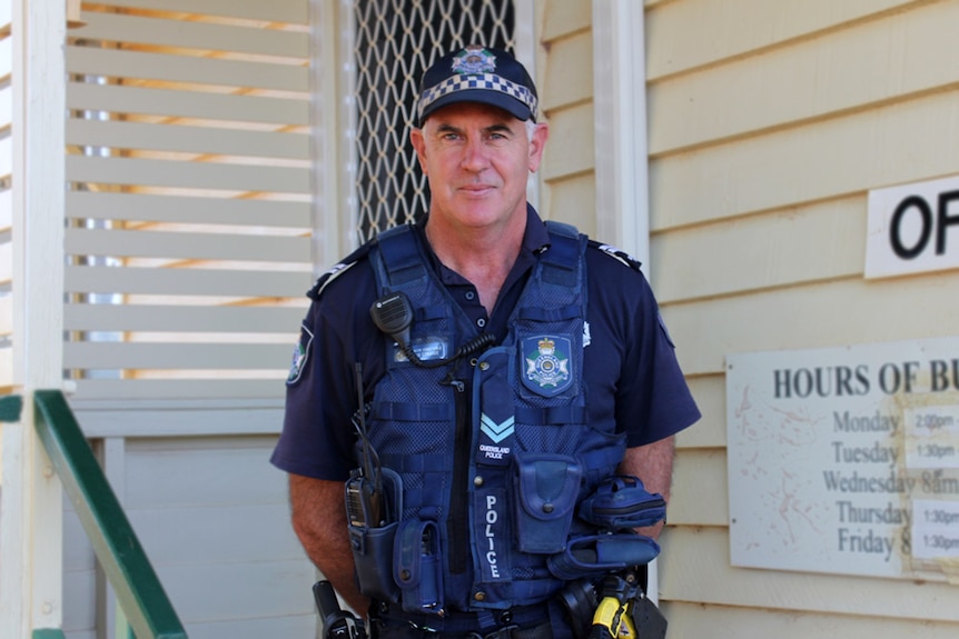 Senior Constable Rob Edwards dressed in uniform, standing  on the doorstep of the Windorah police station.