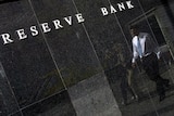 A white collar worker is reflected in the polished black granite facade of the Reserve Bank building in Sydney.