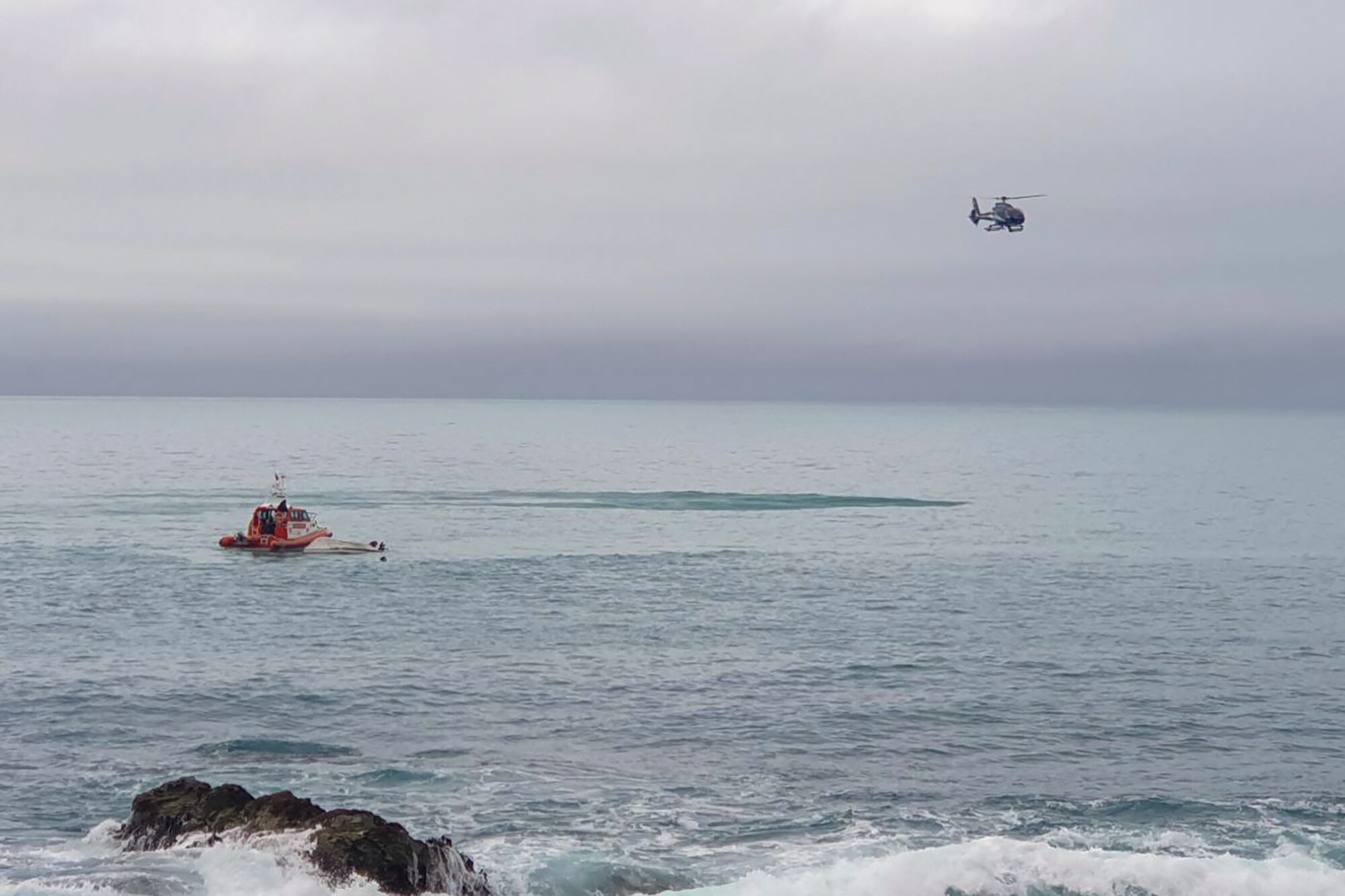 A rescue helicopter circling over a capsized boat 
