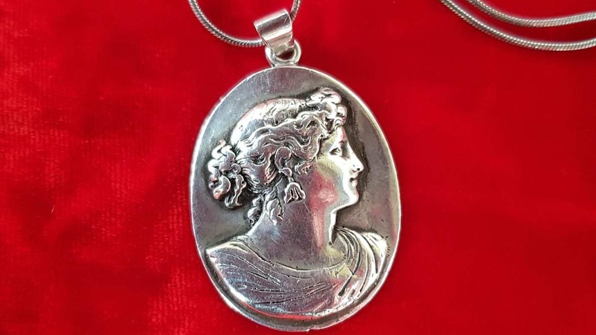 A silver caemo necklace with a chain on a red velvet background.