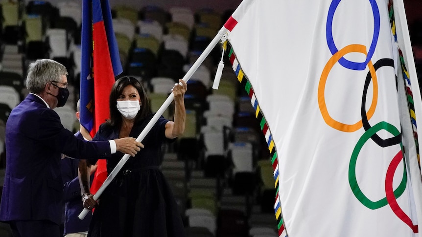 Paris Mayor Anne Hidalgo holds a flag with Olympic rings on it next to IOC president Thomas Bach at the Tokyo closing ceremony.