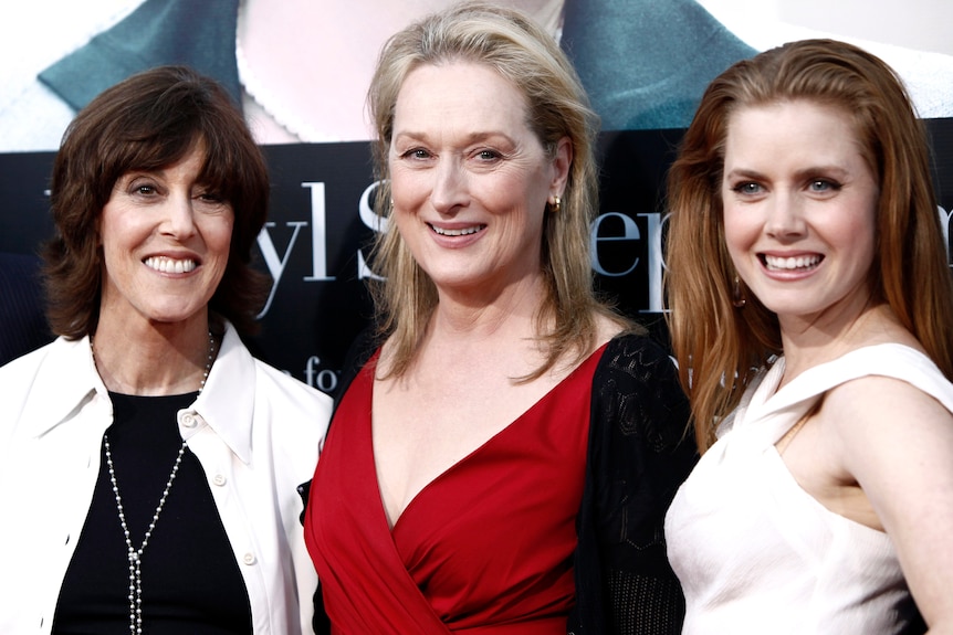 Ephron, Streep and Adams smile together in front of a promotional film poster