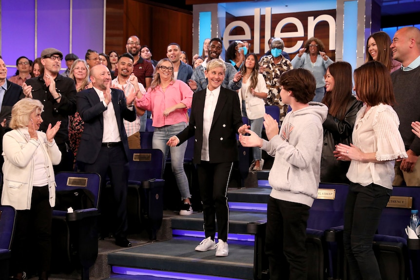 Ellen walks down the stairs smiling as her crowd applauds.