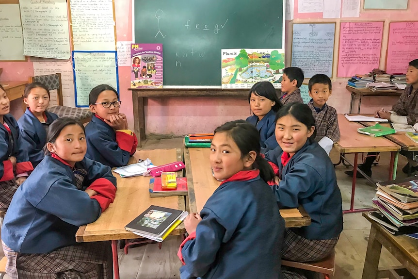 Bhutanese students sit around a table in a classroom looking at books.
