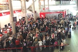 An aerial shot shows long lines of passengers and a makeshift tent where bags were being searched.