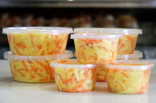 Stacked tubs of cheese slaw on a take away shop counter.