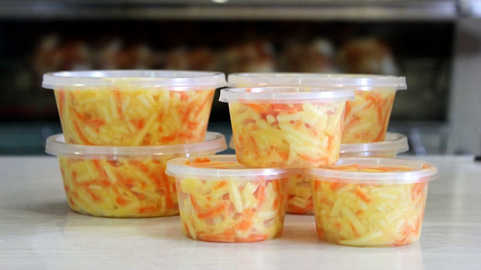 Stacked tubs of cheese slaw on a take away shop counter.