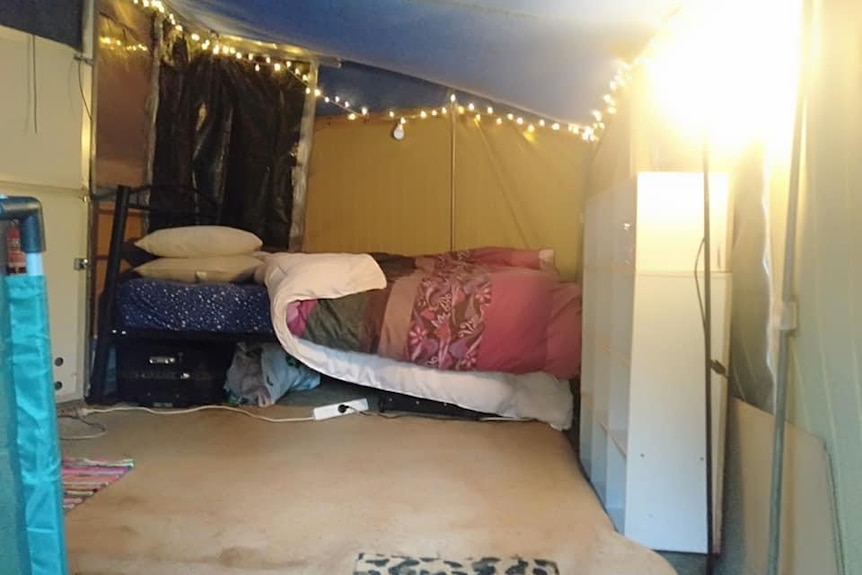 The inside of a caravan annex with a bed, some fairy lights and a dirty cream coloured carpet.