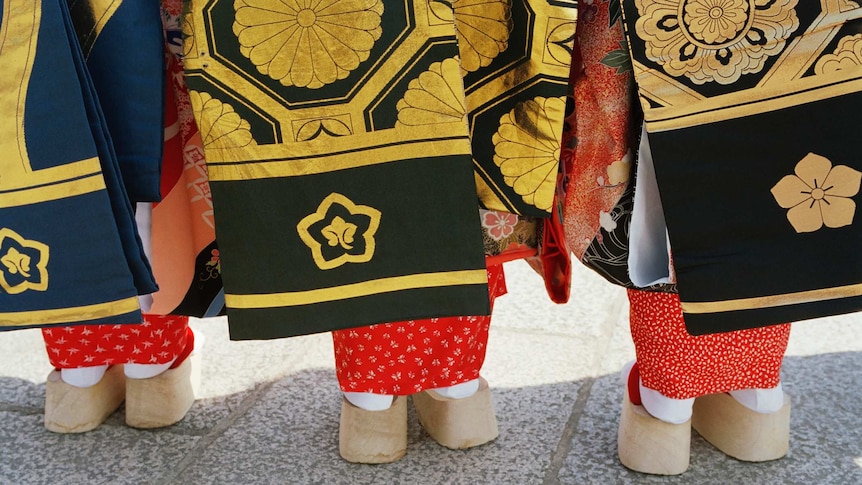 Japan, Kyoto, Three women wearing kimonos standing in row, rear view, low section